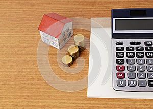 Calculator with notepad and paper house with coins stack