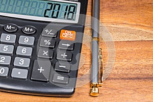 Calculator with 2018 number And Ballpoint Pen Branch On Wooden Table. Close Up