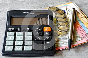 Calculator with number 2024 on display, pen, euro banknotes and coins on grey background