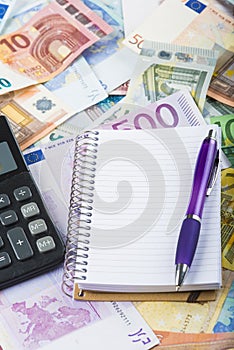 Calculator pen and notebook on the money