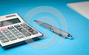 Calculator, pen and table calendar on blue background. Top view of office desk