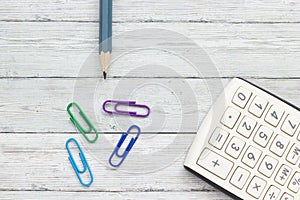 Calculator, pencil and paper clips on a wood background