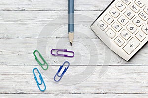 Calculator, pencil and paper clips on a wood background, close-up