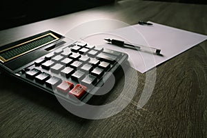 Calculator and pencil and white paper on a wooden desk. Calculation concept selective focus