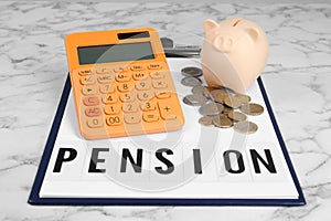 Calculator, piggy bank, coins and clipboard with word Pension on white marble table. Retirement concept