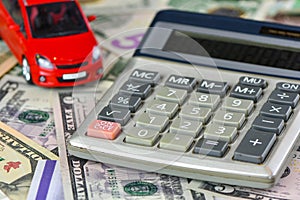 Calculator and red toy car on a variety of national currency banknotes background.  Concept of the cost of purchasing, renting and