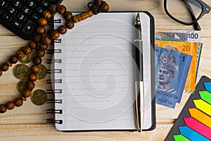 Calculator, rosary, coins, banknotes, book, spectacle and pen on wooden background