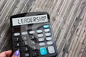 Calculator in a woman\'s hand showing the word leadership on a wooden table. Business leadership and management concept