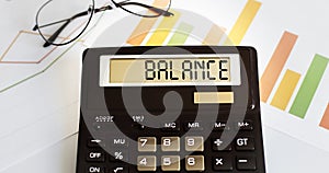 Calculator with the word BALANCE on the display with chart and glasses