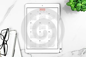 Calendar 2022. Tablet computer with open app. White marble background, business desktop, to do goals and planning for
