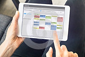 Calendar app on tablet computer with planning of the week with appointments, events, tasks, and meeting. Hands holding device,