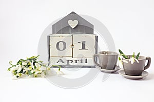 Calendar for April 1 :cubes with the numbers 01, the name of the month in English, two gray coffee cups, a bouquet of snowdrops on