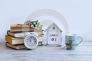 Calendar for April 1: a decorative house with the name of the month April in English, the numbers 01, a stack of books, a bouquet