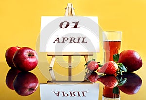 Calendar for April 1: an easel with the inscription 01, april, apples and strawberries next to it, a glass of freshly squeezed