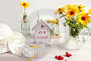 Calendar for August 1: a decorative house with numbers 01, the name of the month of August in English, bouquets of yellow daisies