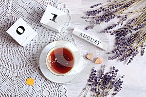 Calendar for August 1 :the name of the month of August in English, cubes with the number 01, a cup of tea on a gray napkin, two