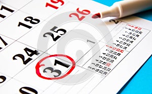 Calendar in close-up on a blue background. Red marker on the calendar. The 31th number in the calendar is circled in red with a