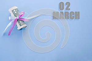Calendar date on blue background with rolled up dollar bills pinned by blue and pink ribbon with copy space.  March 2 is the