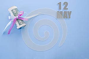 Calendar date on blue background with rolled up dollar bills pinned by blue and pink ribbon with copy space. May 12 is the twelfth