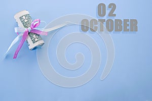 Calendar date on blue background with rolled up dollar bills pinned by blue and pink ribbon with copy space. October 2 is the