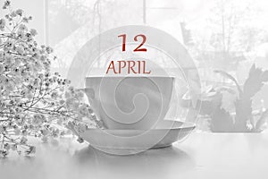 Calendar date on light background with porcelain white tea pair and white gypsophila with copy space. April 12 is the twelfth day