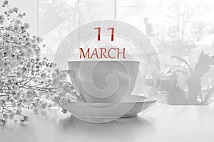 Calendar date on light background with porcelain white tea pair and white gypsophila with copy space. March 11 is the eleventh