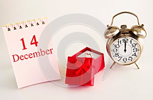 Calendar date on light background with red gift box with ring and alarm clock with copy space. December 14 is the fourteenth  day