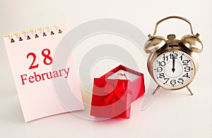 Calendar date on light background with red gift box with ring and alarm clock with copy space.