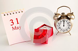 Calendar date on light background with red gift box with ring and alarm clock with copy space.