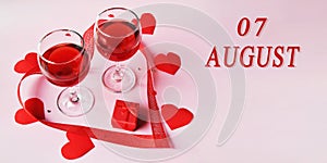 calendar date on light background with two glasses of red wine, red gift box and red hearts with copy space. August 7 is