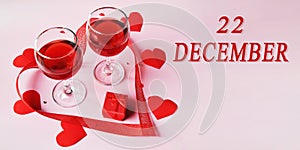 calendar date on light background with two glasses of red wine, red gift box and red hearts with copy space. December 22
