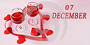 calendar date on light background with two glasses of red wine, red gift box and red hearts with copy space. December 7