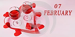 calendar date on light background with two glasses of red wine, red gift box and red hearts with copy space. February 7