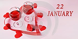 calendar date on light background with two glasses of red wine, red gift box and red hearts with copy space. January 22