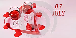 calendar date on light background with two glasses of red wine, red gift box and red hearts with copy space. July 7 is