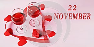 calendar date on light background with two glasses of red wine, red gift box and red hearts with copy space. November 22