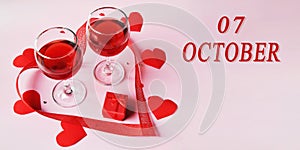 calendar date on light background with two glasses of red wine, red gift box and red hearts with copy space. October 7