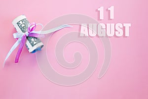 Calendar date on pink background with rolled up dollar bills pinned by pink and blue ribbon with copy space. August 11 is the