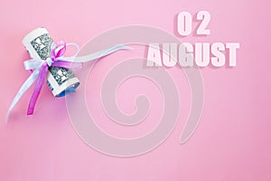 Calendar date on pink background with rolled up dollar bills pinned by pink and blue ribbon with copy space.  August 2 is the