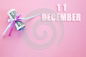 Calendar date on pink background with rolled up dollar bills pinned by pink and blue ribbon with copy space. December 11 is the