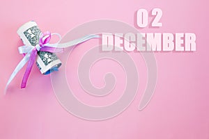 Calendar date on pink background with rolled up dollar bills pinned by pink and blue ribbon with copy space.  December 2 is the