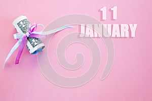 Calendar date on pink background with rolled up dollar bills pinned by pink and blue ribbon with copy space. January 11 is the