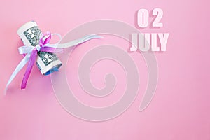 Calendar date on pink background with rolled up dollar bills pinned by pink and blue ribbon with copy space. July 2 is the second