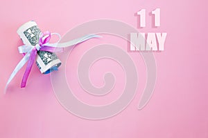 Calendar date on pink background with rolled up dollar bills pinned by pink and blue ribbon with copy space. May 11 is the