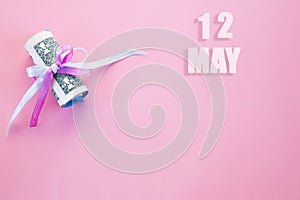 Calendar date on pink background with rolled up dollar bills pinned by pink and blue ribbon with copy space. May 12 is the twelfth
