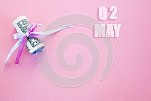 Calendar date on pink background with rolled up dollar bills pinned by pink and blue ribbon with copy space. May 2 is the second
