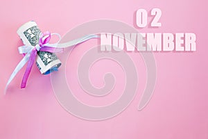 Calendar date on pink background with rolled up dollar bills pinned by pink and blue ribbon with copy space. November 2 is the