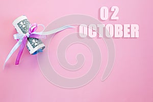 Calendar date on pink background with rolled up dollar bills pinned by pink and blue ribbon with copy space. October 2 is the