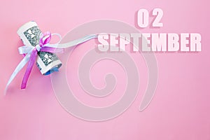 Calendar date on pink background with rolled up dollar bills pinned by pink and blue ribbon with copy space.  September 2 is the