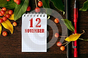 calendar date on wooden dark desktop background with autumn leaves and small apples. November 12 is the twelfth day of the month